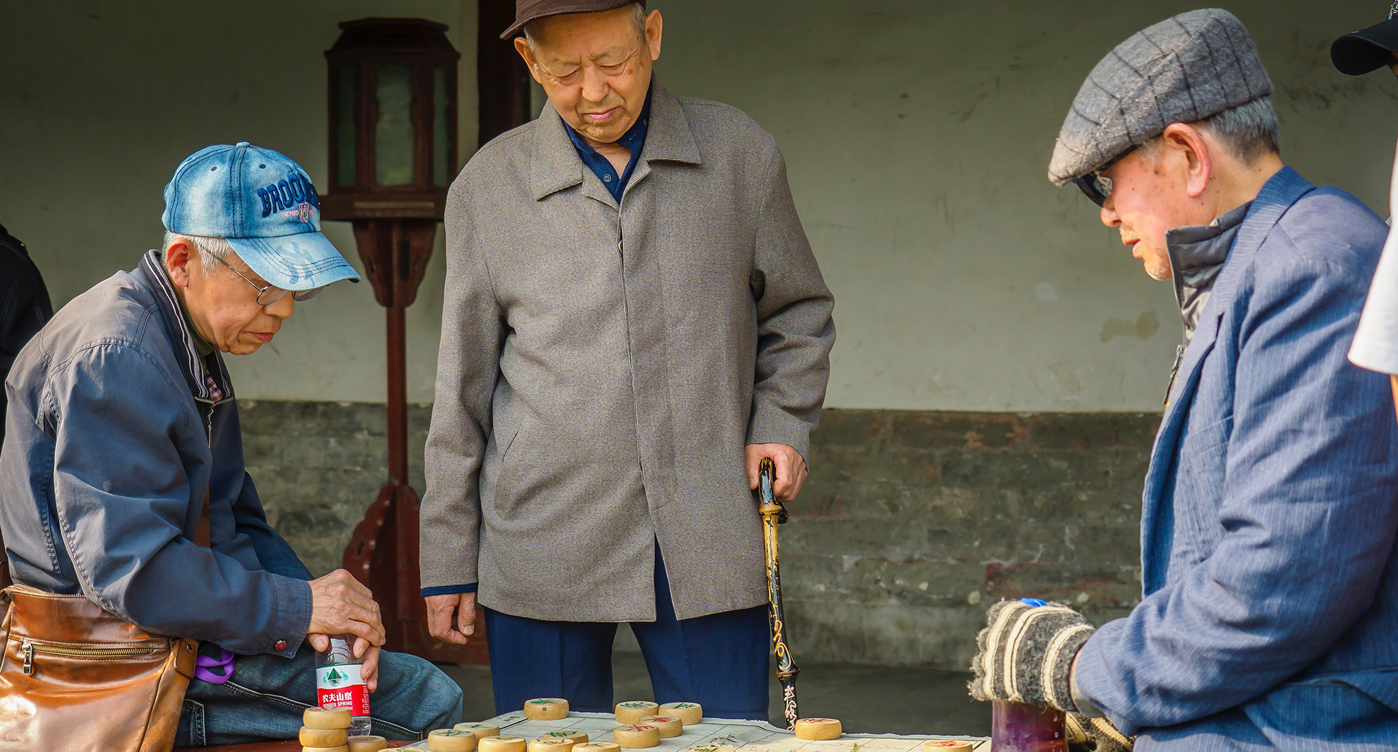 Three elderly men playing a Chinese board game outside.